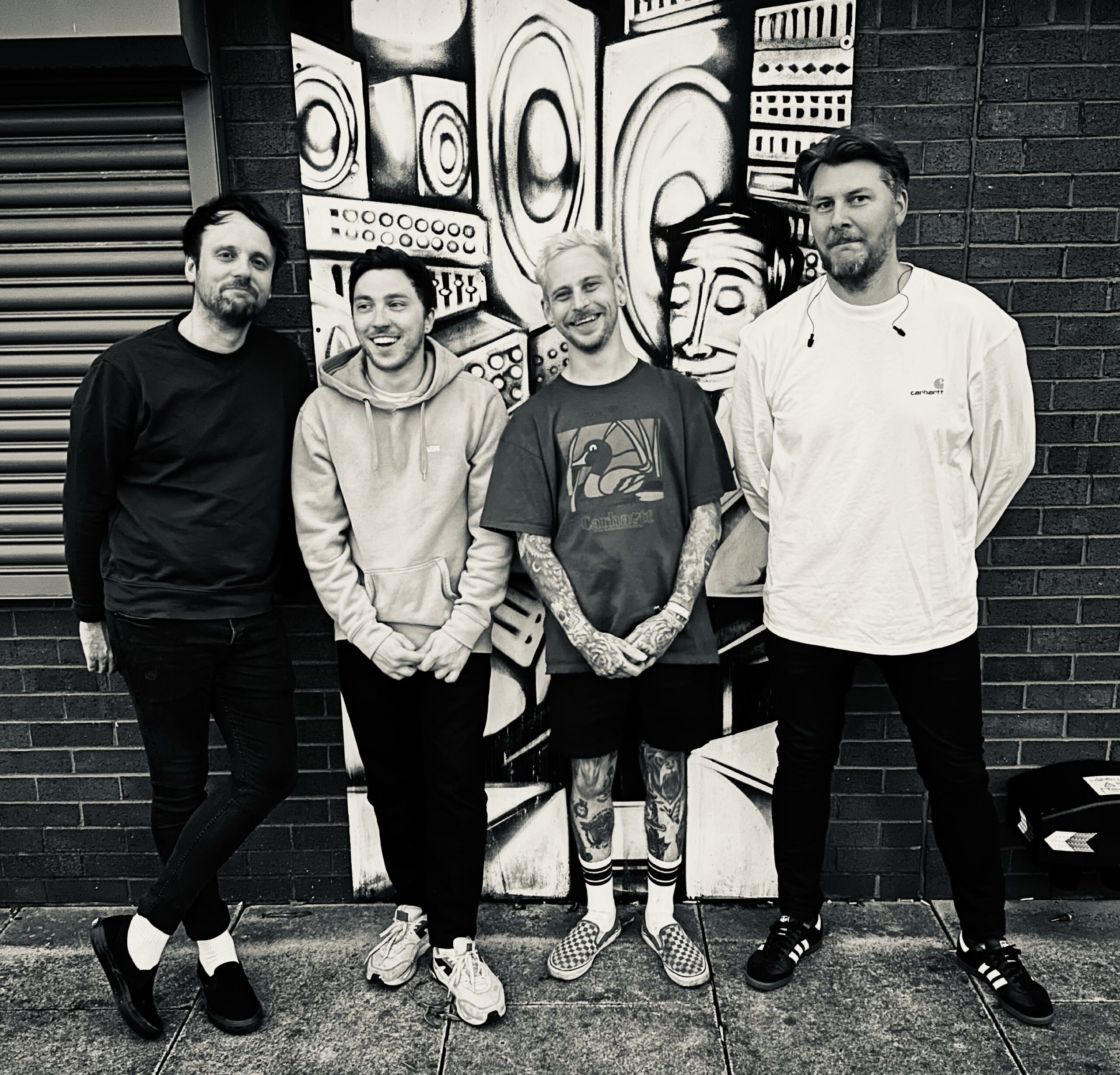 Black and white image of four males standing in front of a mural.